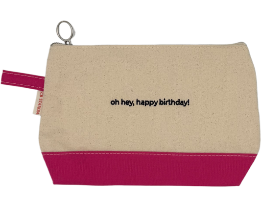 Beige pouch with pink bottom section and 'oh hey, happy birthday!' text on a white background